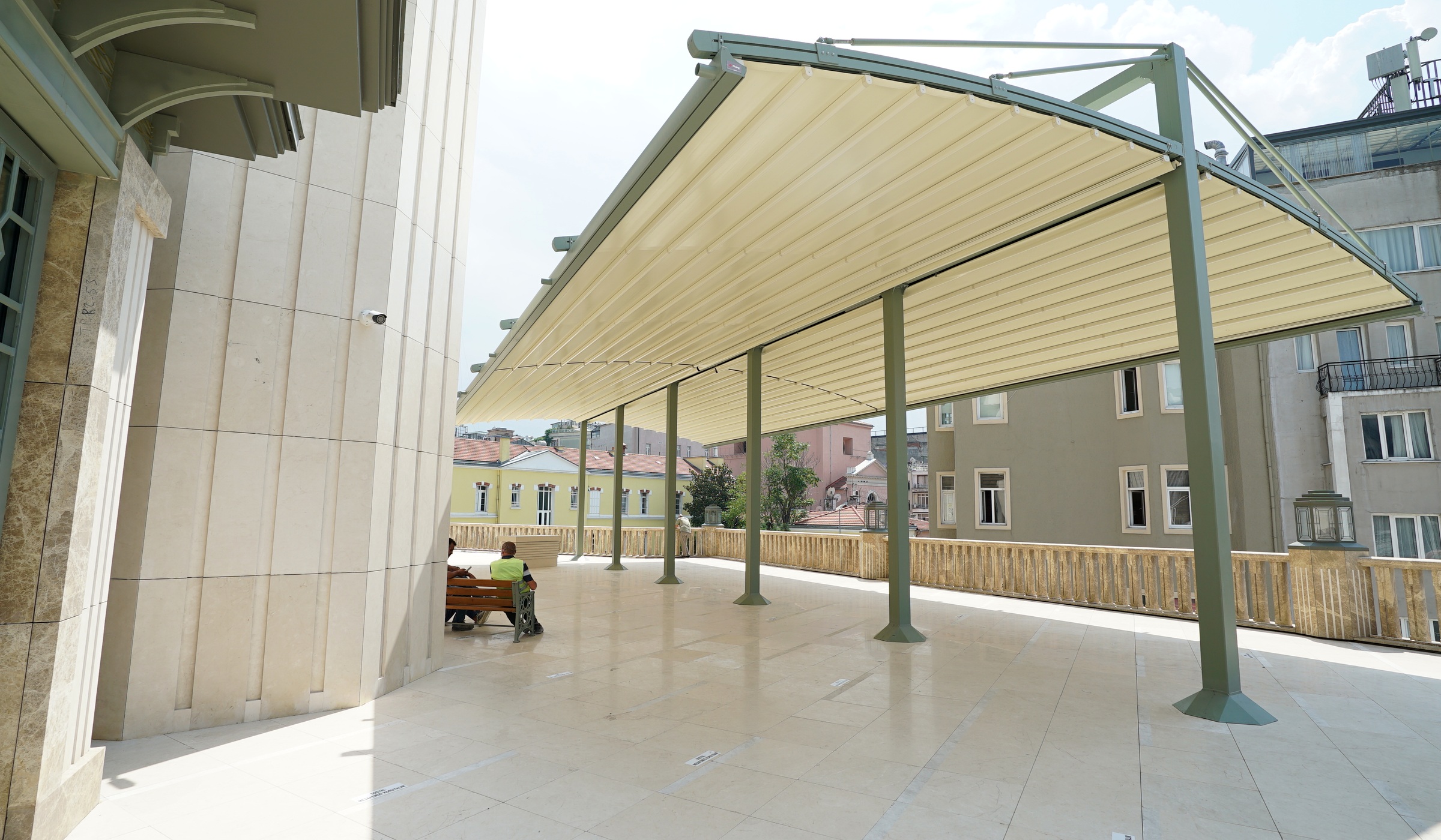 Free standing fabric roof structure with curved arms over a public terrace